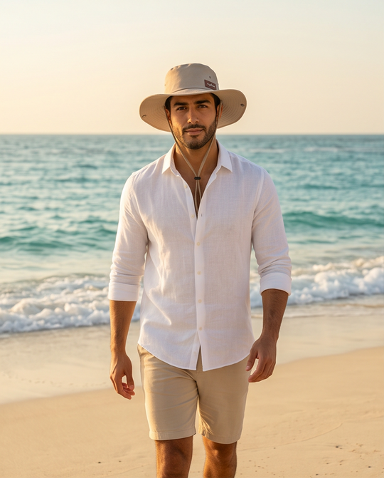 Man wearing a white shirt, beige shorts, and a hat on a beach with ocean in the background Malibu Beige Bucket Hat With Rope -ماليبو -
